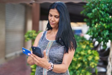 Orta yaşlı İspanyol kadın akıllı telefon ve kredi kartı kullanıyor.