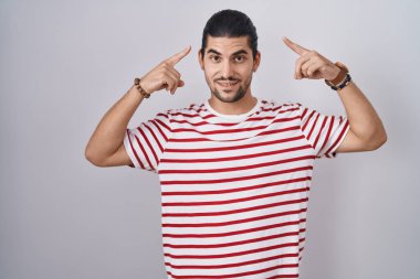 Hispanic man with long hair standing over isolated background smiling pointing to head with both hands finger, great idea or thought, good memory 