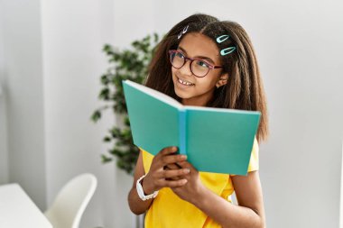 Afro-Amerikalı kız gülümseyerek evde kendinden emin bir şekilde kitap okuyor.