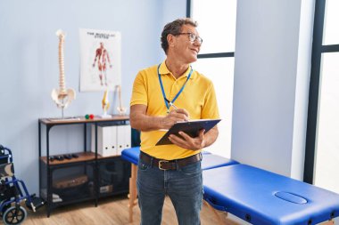 Middle age man physiotherapist writing on clipboard at laundry room