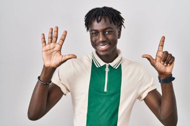 Münzevi arka planda duran Afrikalı adam yedinci parmaklarını gösterip işaret ederken kendinden emin ve mutlu gülümsüyor.. 