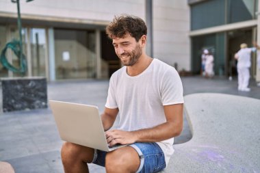 Sokakta dizüstü bilgisayar kullanarak gülümseyen İspanyol genç adam.