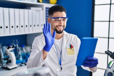 Laboratuvarda çalışan genç yakışıklı adam internette arama yapıyor. Olumlu ve mutlu görünüyor. Kendine güvenen bir gülümsemeyle dişlerini gösteriyor. 