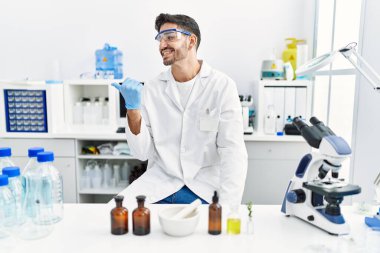 Laboratuvarda çalışan Latin asıllı genç bir adam parmak ucunda ağzı açık gülümsüyor. 