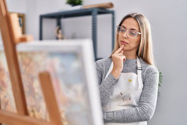 Young woman artist looking draw with doubt expression at art studio