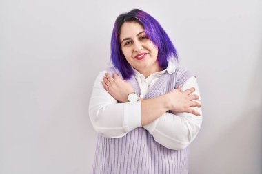 Plus size woman wit purple hair standing over white background hugging oneself happy and positive, smiling confident. self love and self care 
