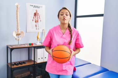 Fizyoterapi kliniğinde çalışan genç bir İspanyol kadın basketbol topu tutuyor. Ağzı ve şaşı gözleriyle balık suratı yapıyor. Deli ve komik.. 