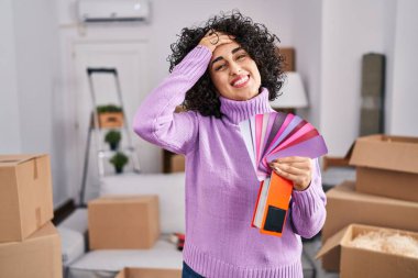 Yeni ev duvarının rengini seçen kıvırcık saçlı, genç esmer kadın. Gergin ve hayal kırıklığına uğramış, şaşırmış ve kızgın yüzlü. 