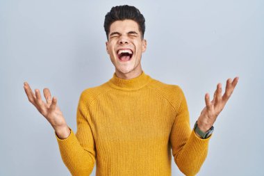 Mavi arka planda duran genç İspanyol adam başarı için deli ve çılgınlığı kutluyor kollarını kaldırmış ve gözlerini kapatmış heyecanla bağırıyor. Kazanan konsept 