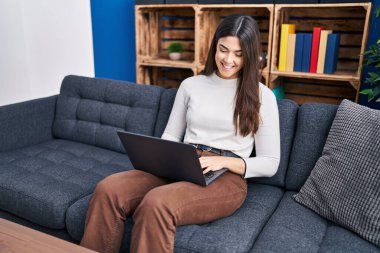 Evdeki kanepede dizüstü bilgisayar kullanan güzel İspanyol kadın.