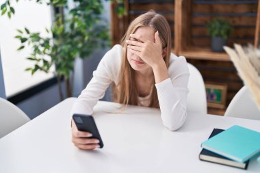 Young caucasian woman using smartphone with serious expression at home
