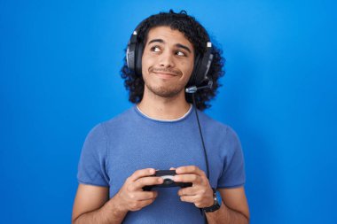 İspanyol asıllı, kıvırcık saçlı, video oyunu oynayan, elinde kumandayla gülümseyen bir adam.. 