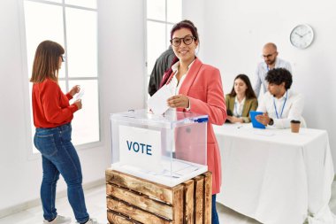 Young voter man smiling happy putting ballot in voting box at vote center.