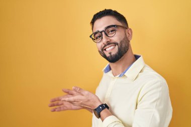 İspanyol genç adam iş kıyafetleri ve gözlük takıp gülümseyerek içeri girmeye davet ediyor. 