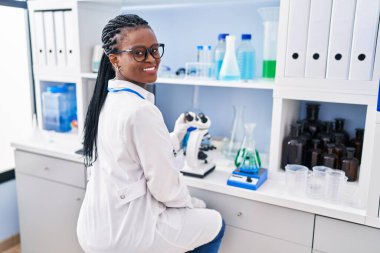 African american woman scientist smiling confident using microscope at laboratory