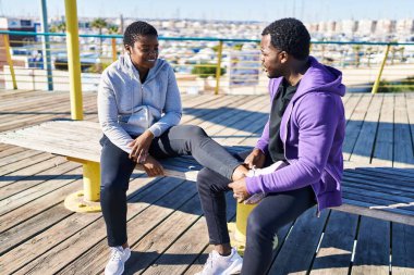 Erkek ve kadın çift spor giyer, bankta oturur, sokakta bileklerine dokunur.