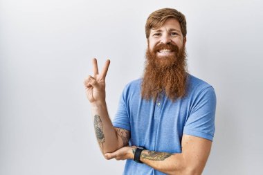 Uzun sakallı beyaz bir adam izole edilmiş arka planda kameraya bakıp gülümsüyor ve zafer işareti yapıyor. İki numara.. 