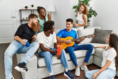 Mutlu gülümseyen ve evde klasik gitar çalan bir grup genç arkadaş..