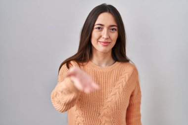 Beyaz arka planda duran esmer bir kadın neşeli bir gülümsemeyle yardım eli uzatıyor ve kabul ediyor.. 