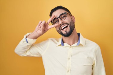 İş kıyafetleri ve gözlük takan İspanyol genç adam barış sembolü yapıyor. Yüzünde parmaklar, gülümseyerek zaferi gösteriyor. 