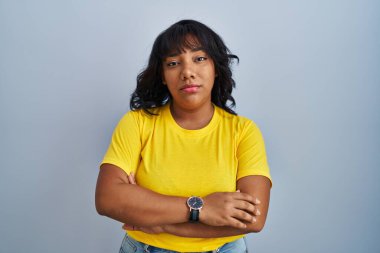 Hispanic woman standing over blue background looking sleepy and tired, exhausted for fatigue and hangover, lazy eyes in the morning. 