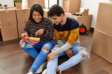 Young latin couple choosing paint color sitting on the floor at new home.