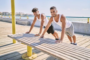 İki İspanyol erkek, deniz kenarında gerinerek gülümsüyor.