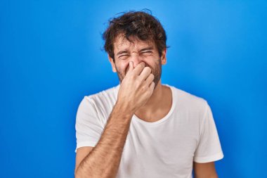 Mavi arka planda dikilen İspanyol genç adam pis ve iğrenç bir koku alıyor. Nefesini burnunda tutuyor. Kötü kokuyor. 