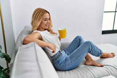 Genç sarışın, kendine güvenen, evde kahve içen.