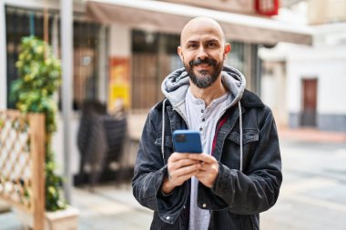 Sokakta akıllı telefon kullanarak kendine güvenen genç kel adam.