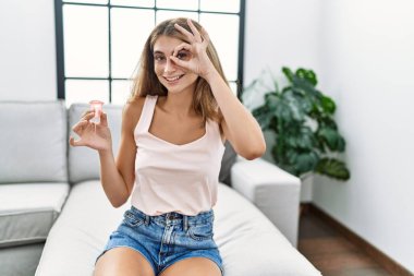 Genç sarışın kadın, elinde regl fincanı tutarken gülümsüyor. 