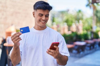 Genç İspanyol adam akıllı telefon ve kredi kartı kullanıyor.