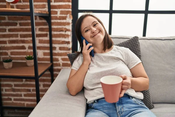 Down syndrome woman drinking coffee and talking on the smartphone at home