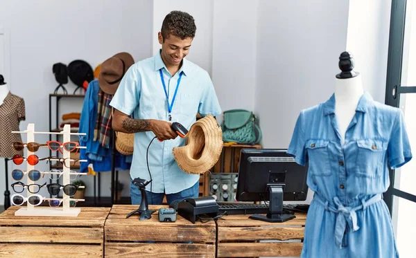 Young hispanic man working as shop assistant selling hat at retail shop