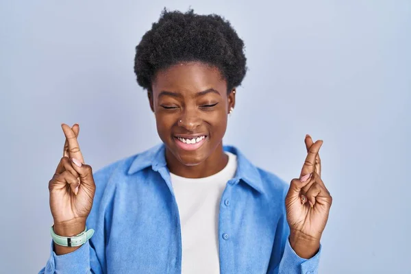 Африканская Американка Стоящая Синем Фоне Жестом Скрестила Пальцы Улыбаясь Закрытыми — стоковое фото