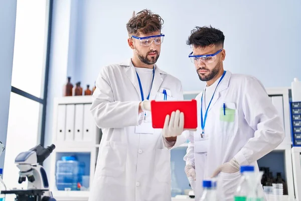 Young couple wearing scientist uniform using touchpad at laboratory
