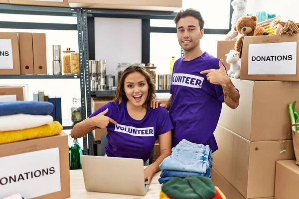 Young hispanic people wearing volunteer t shirt at donations stand smiling happy pointing with hand and finger