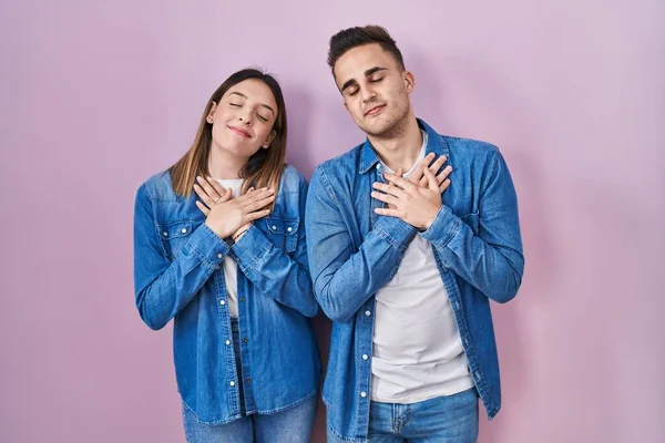 Young Hispanic Couple Standing Pink Background Smiling Hands Chest Closed — Stockfoto