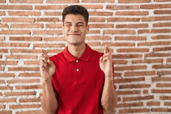 Joven Hombre Hispano Pie Sobre Pared Ladrillos Gesto Dedo Cruzado — Foto de Stock