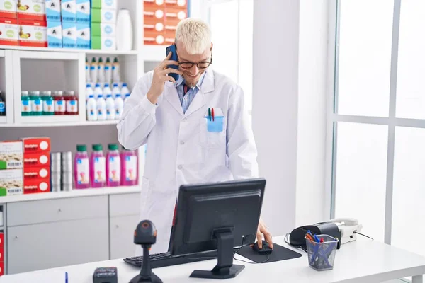 年轻的高加索男子药剂师在药店用电脑用智能手机交谈 — 图库照片