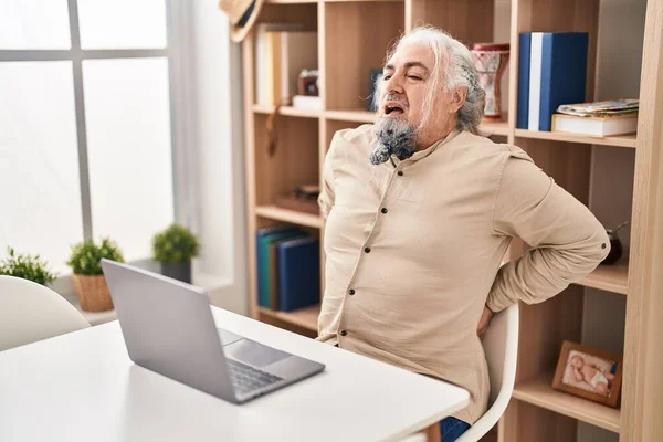 中年白髪の男苦しみのために腰痛使用ノートパソコンの上に座ってテーブルに家 — ストック写真