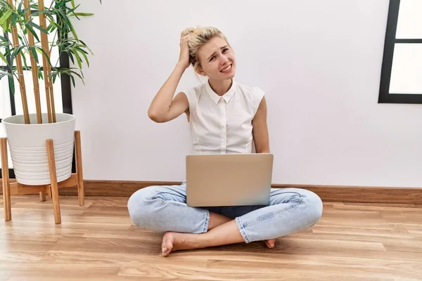 年轻的金发女人坐在客厅的地板上 用电脑笔记本电脑 对问题感到困惑和好奇 拿不定主意 手拿着头思考 沉思的概念 — 图库照片