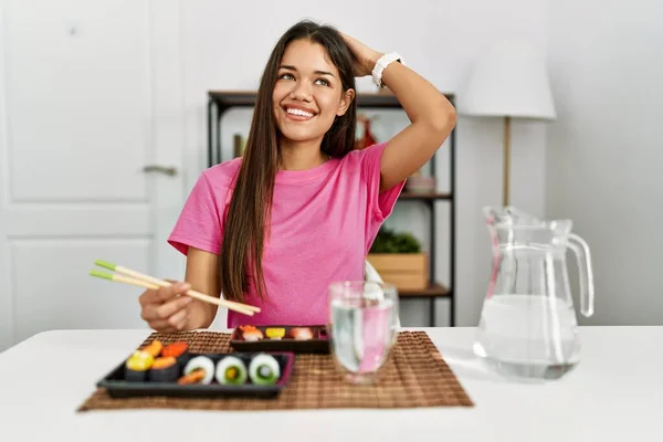 若いブルネットの女性食べる寿司箸を使用して自信を持って触れる髪に手をジェスチャーで笑顔 魅力的でファッショナブルなポーズ — ストック写真