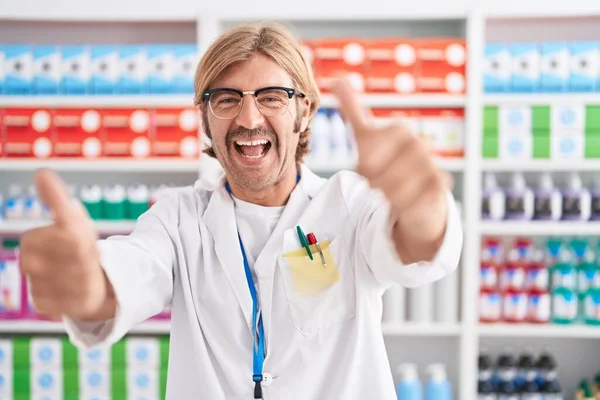 薬局で働く口ひげを持つ白人男性は 手で積極的なジェスチャーを行うことを承認します 親指アップ笑顔と成功のために幸せ 勝者のジェスチャー — ストック写真