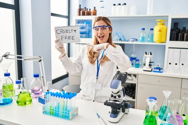 Young blonde scientist woman working on cruelty free laboratory smiling happy pointing with hand and finger