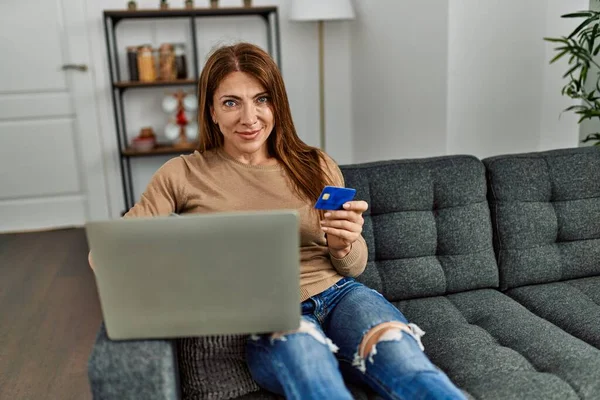 自宅でソファに座っているスマートフォンやクレジットカードを使用して中世の白人女性 — ストック写真