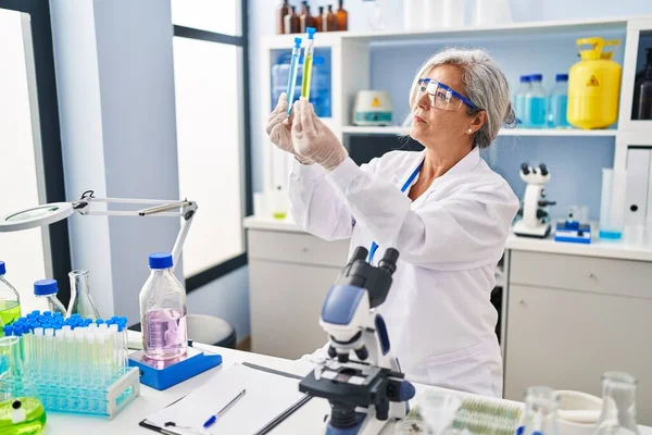中年妇女穿着科学家制服在实验室里看试管 — 图库照片