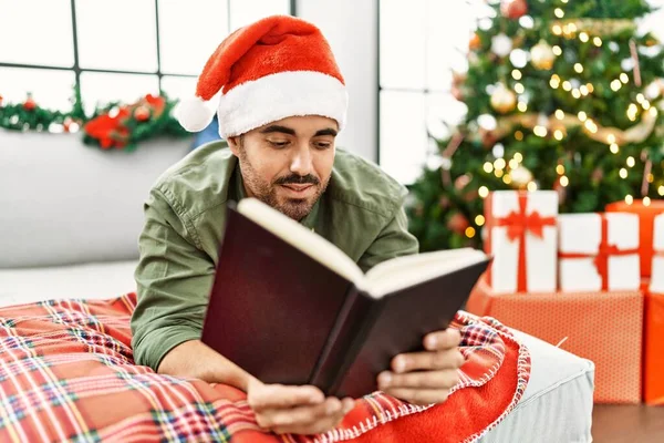 Young Hispanic Man Reading Book Lying Sofa Christmas Tree Home — Stok fotoğraf