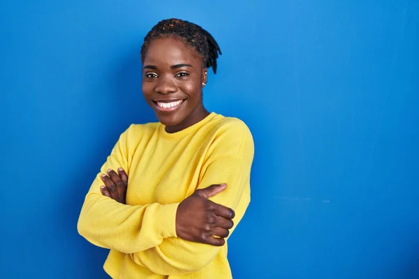 Beautiful black woman standing over blue background happy face smiling with crossed arms looking at the camera. positive person.
