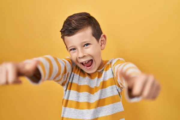 黄色の背景に立っている若い白人の子供は 手で積極的なジェスチャーを行うことを承認し 親指を上げて笑顔と成功のために幸せ 勝者のジェスチャー — ストック写真